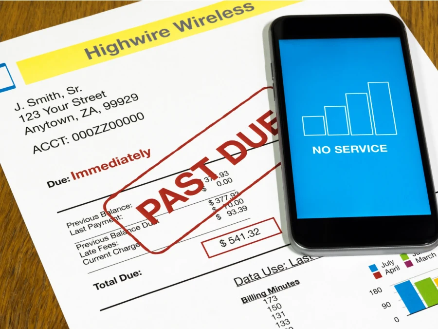 a past due bill on a brown wood table with a cell phone that says "no service".