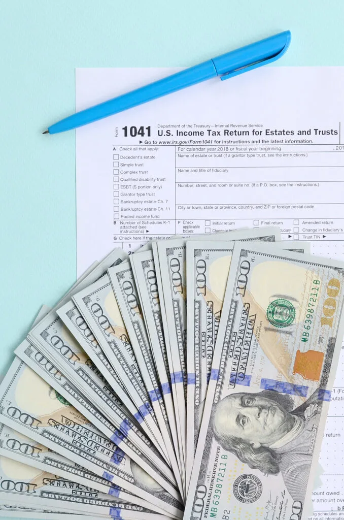 tax forms with hundred dollar bills laying on blue table
